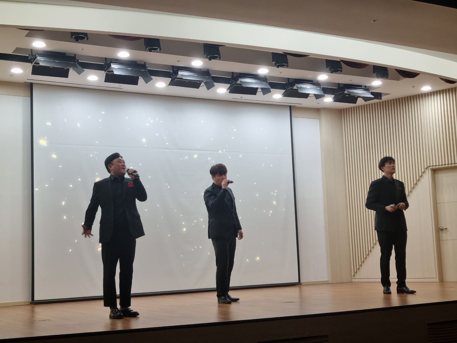 기업 강당 무대에서 노래하는 성악가 세 명